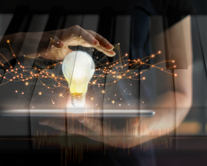 6 Hand holding a glowing light bulb over a laptop, with a network of orange lines and dots surrounding the bulb